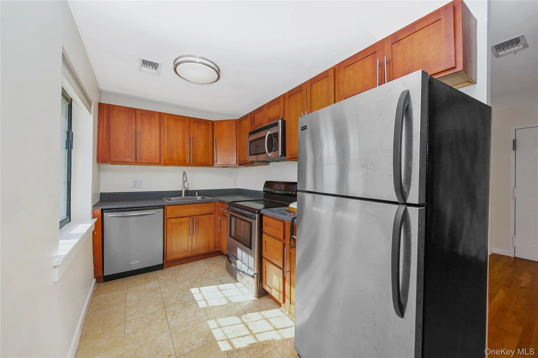 Kitchen featuring stainless steel appliances, dark countertops, brown cabinets, and light tile patterned floors Kitchen featuring stainless steel appliances, dark countertops, brown cabinets, and light tile patterned floors