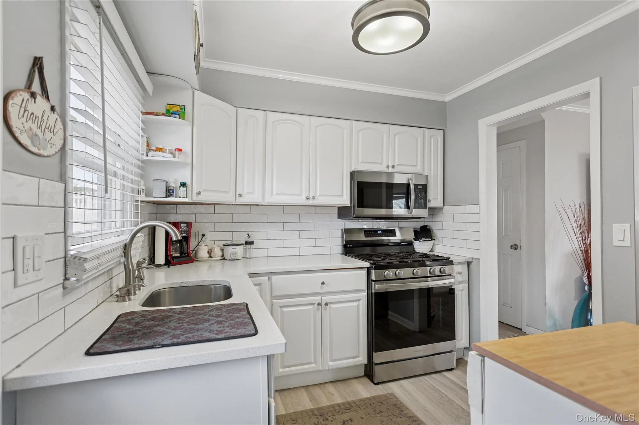 Kitchen with appliances with stainless steel finishes, white cabinetry, backsplash, ornamental molding, and open shelves Kitchen with appliances with stainless steel finishes, white cabinetry, backsplash, ornamental molding, and open shelves