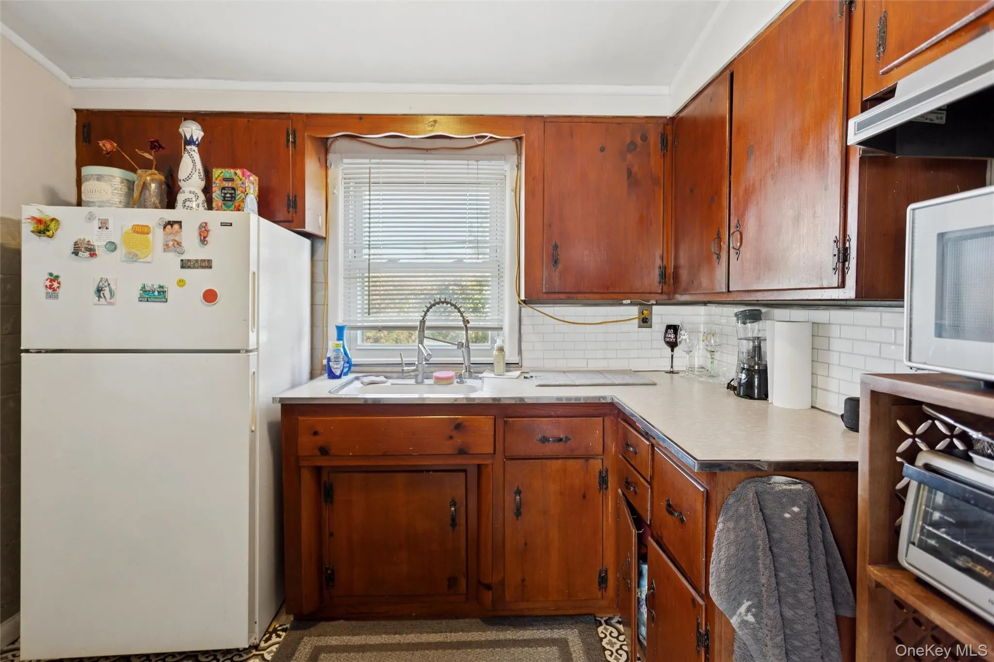 Kitchen with white appliances, under cabinet range hood, light countertops, decorative backsplash, and brown cabinets Kitchen with white appliances, under cabinet range hood, light countertops, decorative backsplash, and brown cabinets
