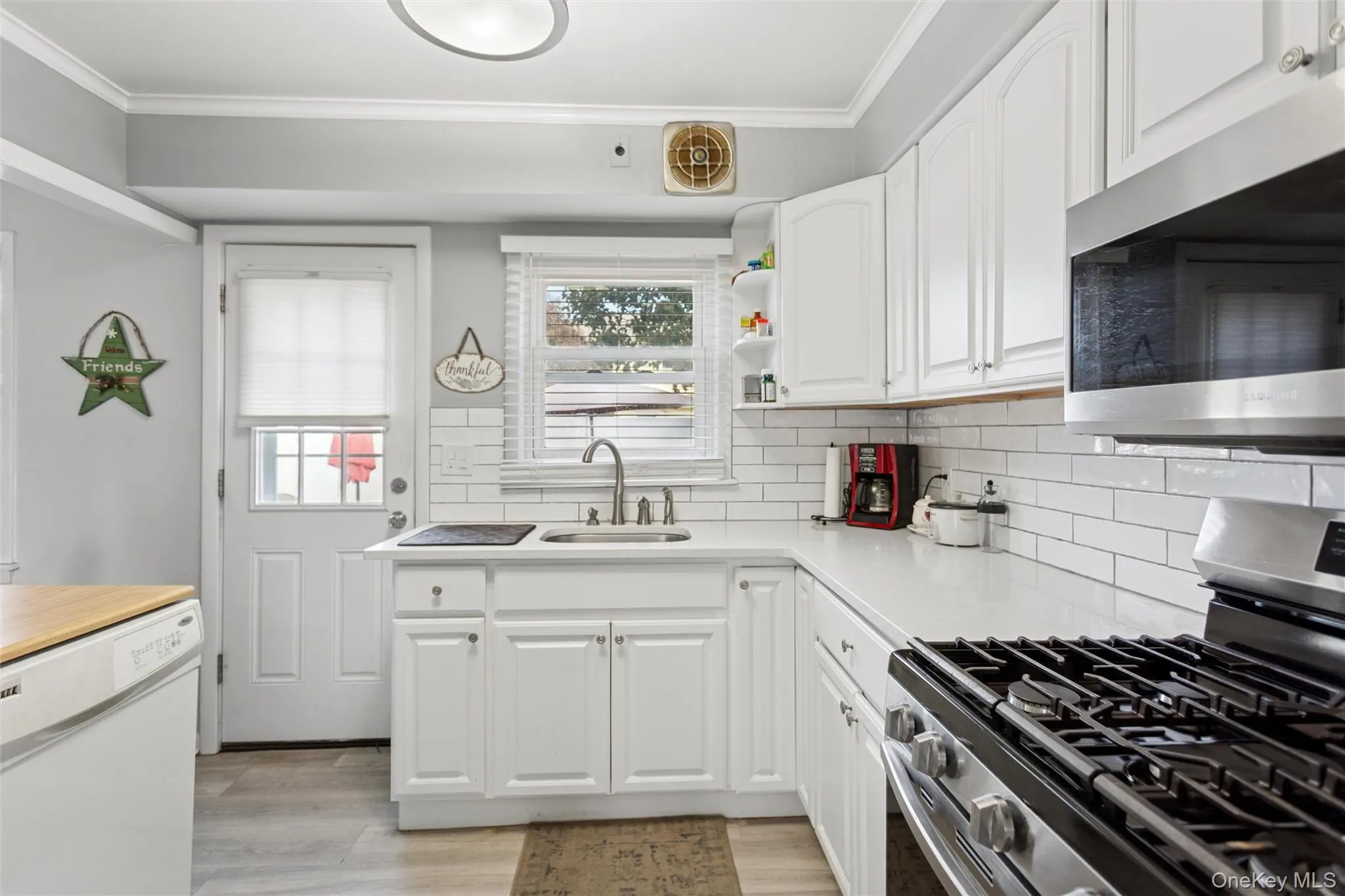 Kitchen featuring appliances with stainless steel finishes, tasteful backsplash, white cabinetry, ornamental molding, and open shelves Kitchen featuring appliances with stainless steel finishes, tasteful backsplash, white cabinetry, ornamental molding, and open shelves