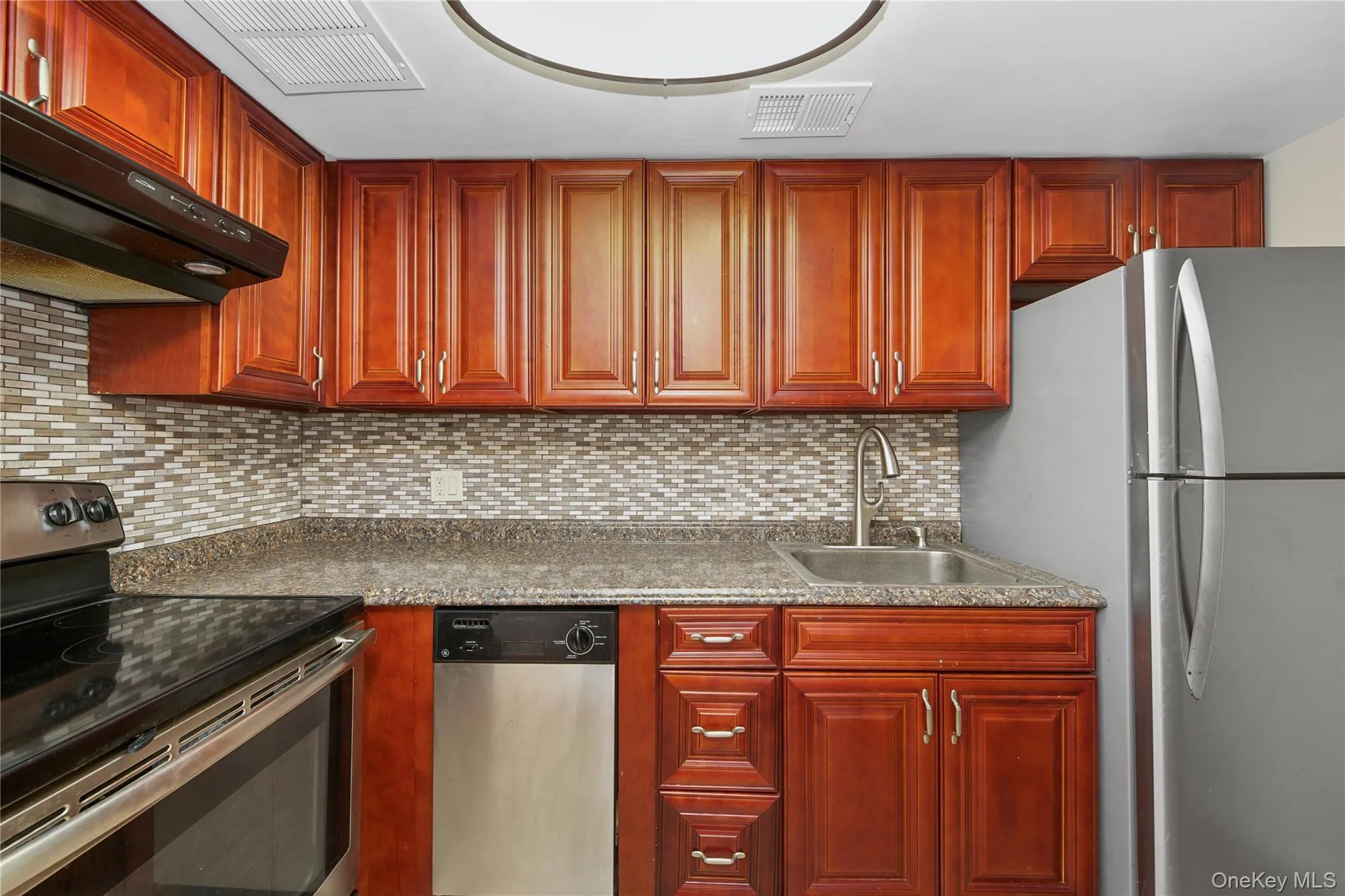 Kitchen with appliances with stainless steel finishes, backsplash, dark brown cabinets, and ventilation hood Kitchen with appliances with stainless steel finishes, backsplash, dark brown cabinets, and ventilation hood