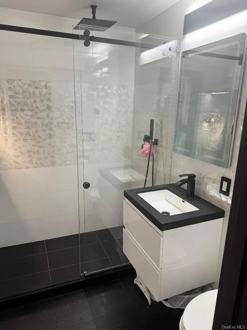Full bath featuring tile walls, vanity, a shower stall, and dark tile patterned flooring Full bath featuring tile walls, vanity, a shower stall, and dark tile patterned flooring