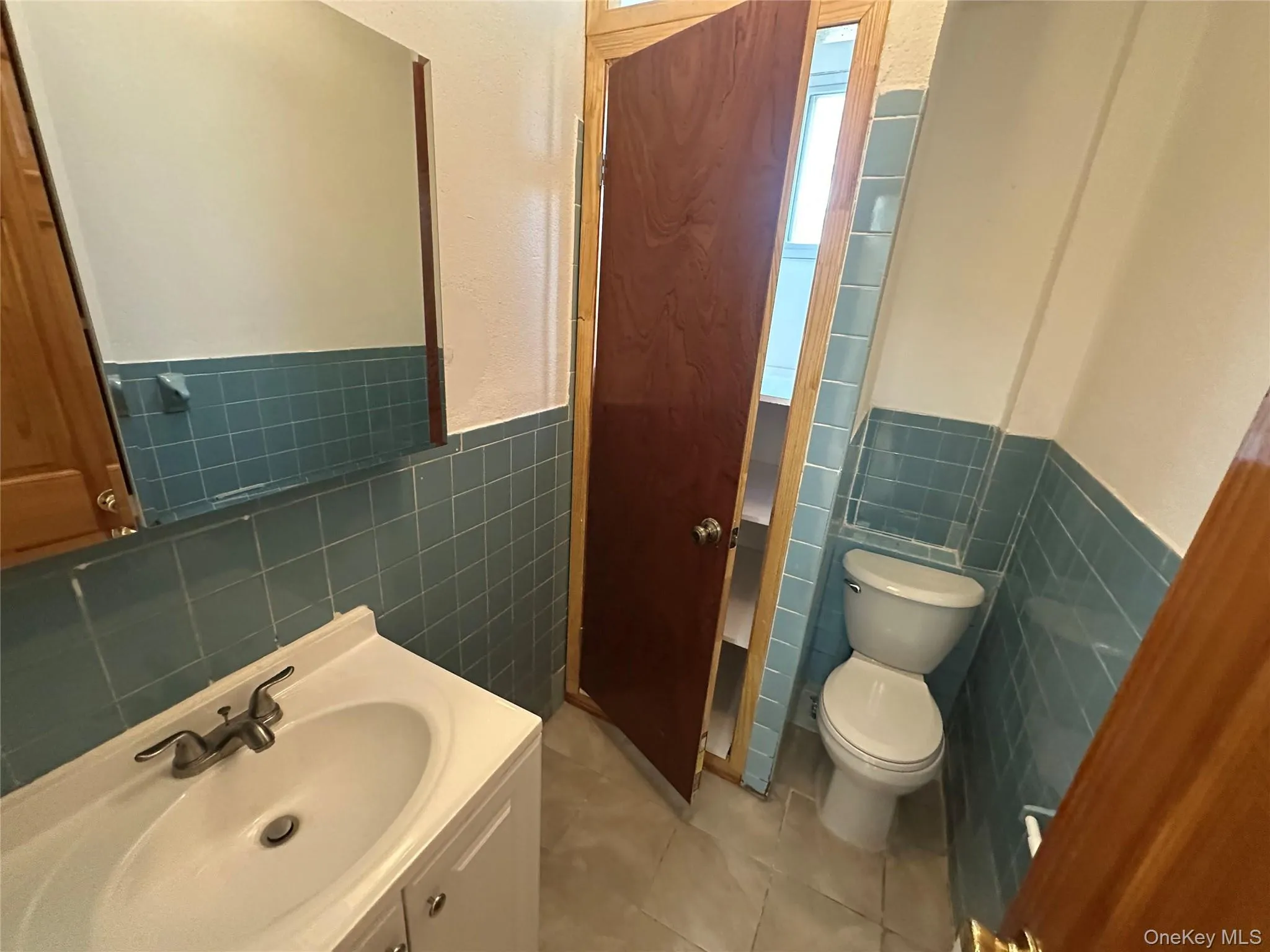 Bathroom with light tile patterned floors, vanity, tile walls, and a wainscoted wall Bathroom with light tile patterned floors, vanity, tile walls, and a wainscoted wall