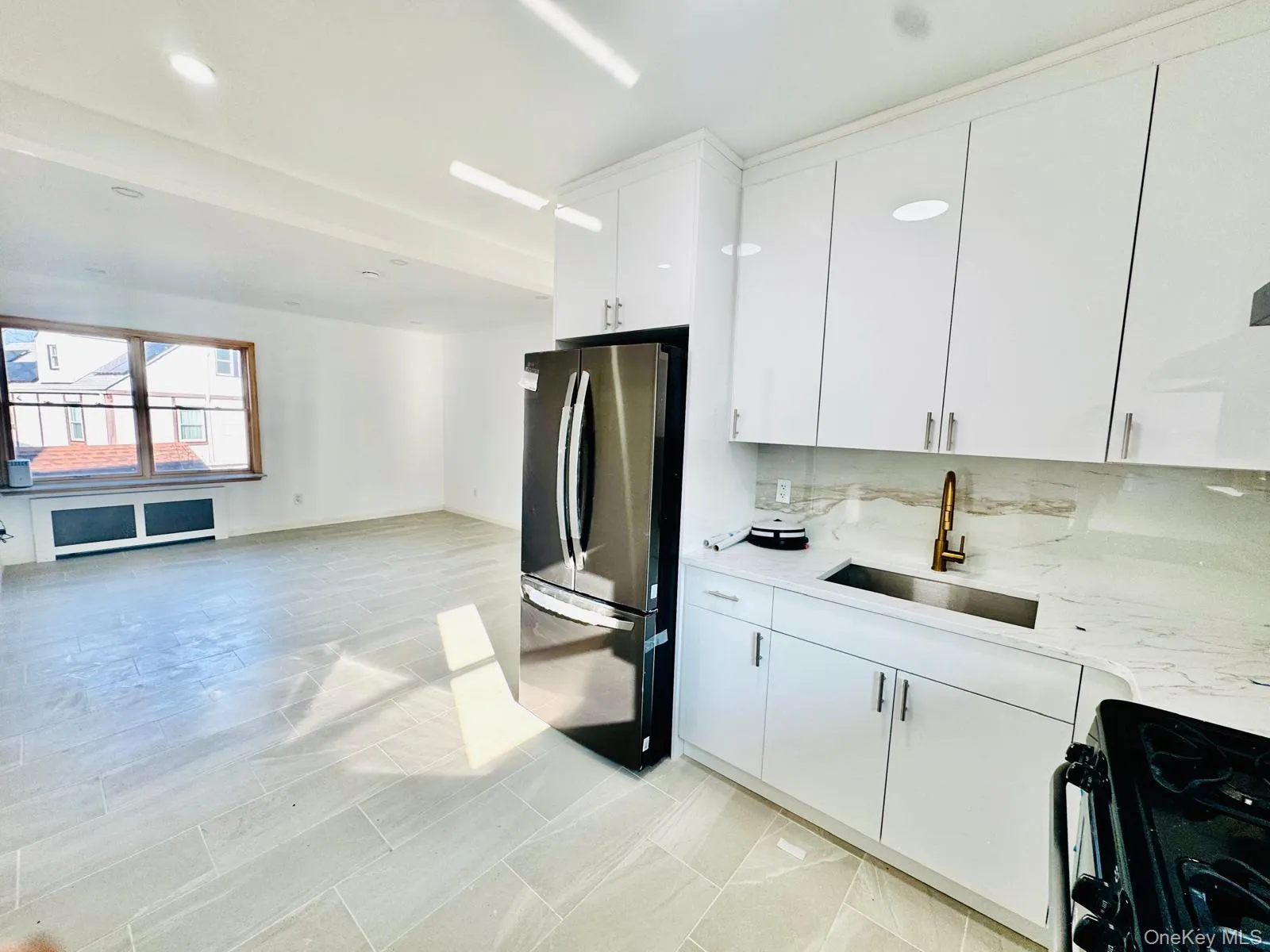 Kitchen with freestanding refrigerator, black gas stove, white cabinetry, decorative backsplash, and light stone counters Kitchen with freestanding refrigerator, black gas stove, white cabinetry, decorative backsplash, and light stone counters