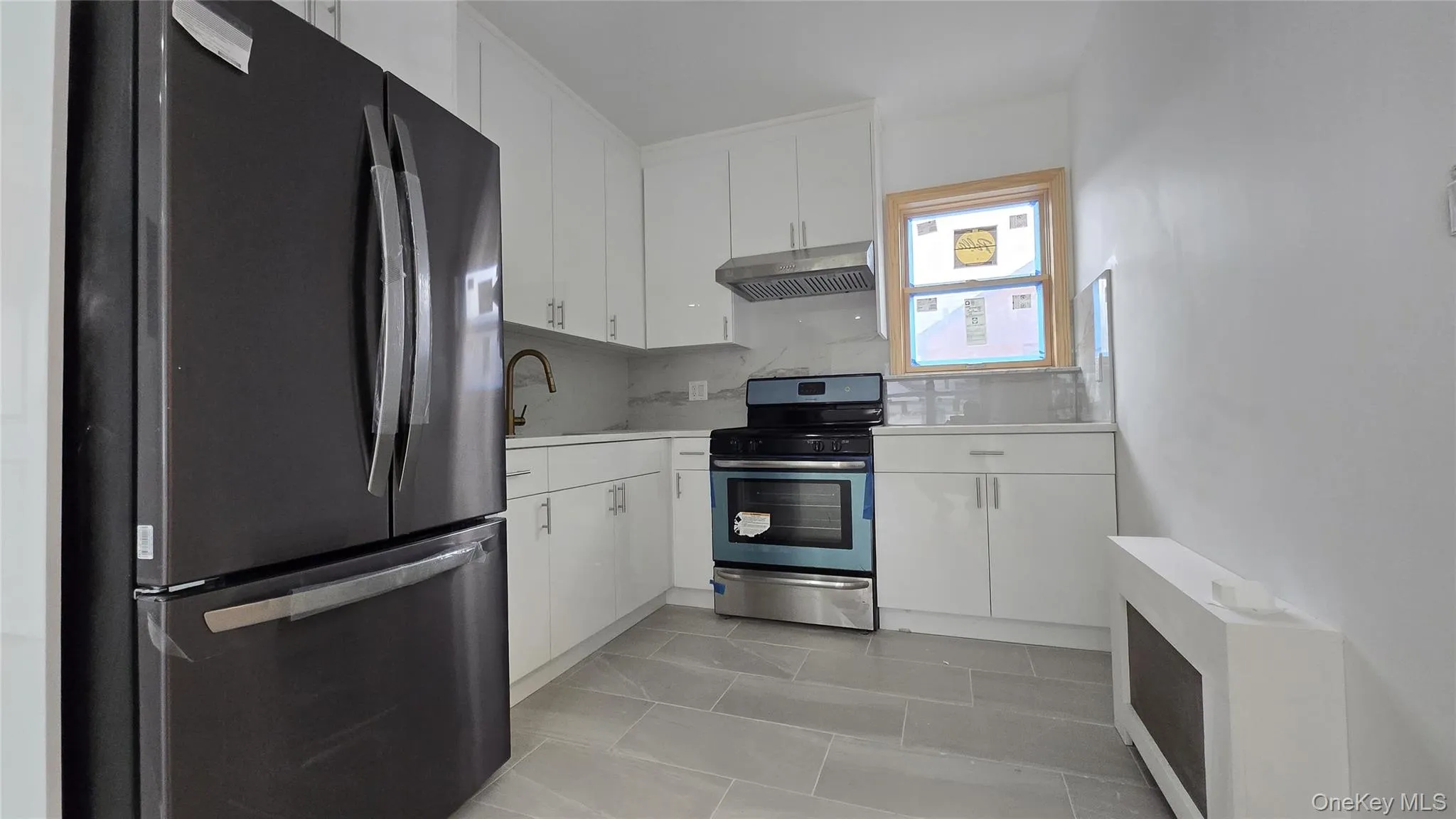 Kitchen with stainless steel appliances, white cabinets, radiator heating unit, under cabinet range hood, and backsplash Kitchen with stainless steel appliances, white cabinets, radiator heating unit, under cabinet range hood, and backsplash