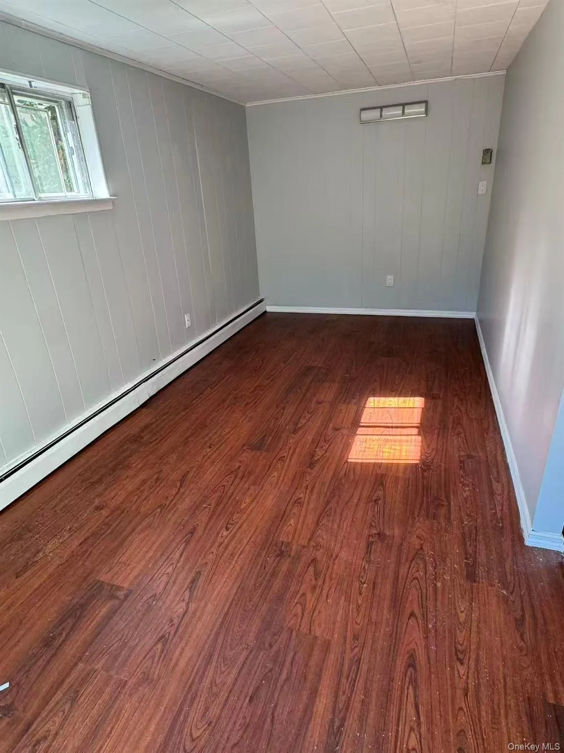 Unfurnished room with baseboard heating, dark wood-style floors, and wooden walls Unfurnished room with baseboard heating, dark wood-style floors, and wooden walls