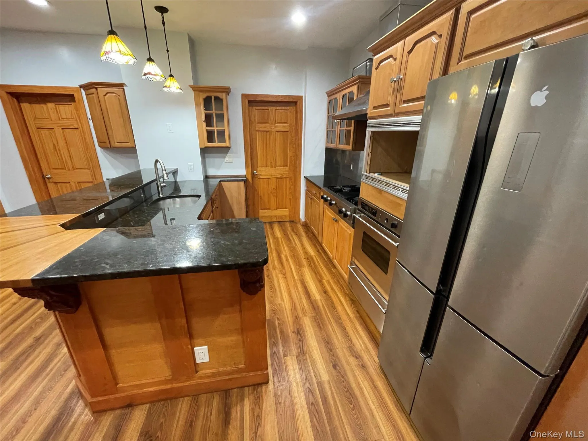 Kitchen featuring glass insert cabinets, brown cabinetry, stainless steel appliances, pendant lighting, and recessed lighting Kitchen featuring glass insert cabinets, brown cabinetry, stainless steel appliances, pendant lighting, and recessed lighting