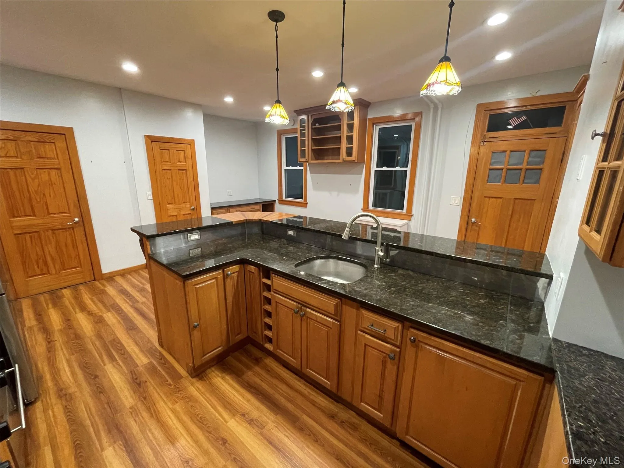 Kitchen featuring brown cabinets, dark stone countertops, light wood-style floors, pendant lighting, and recessed lighting Kitchen featuring brown cabinets, dark stone countertops, light wood-style floors, pendant lighting, and recessed lighting