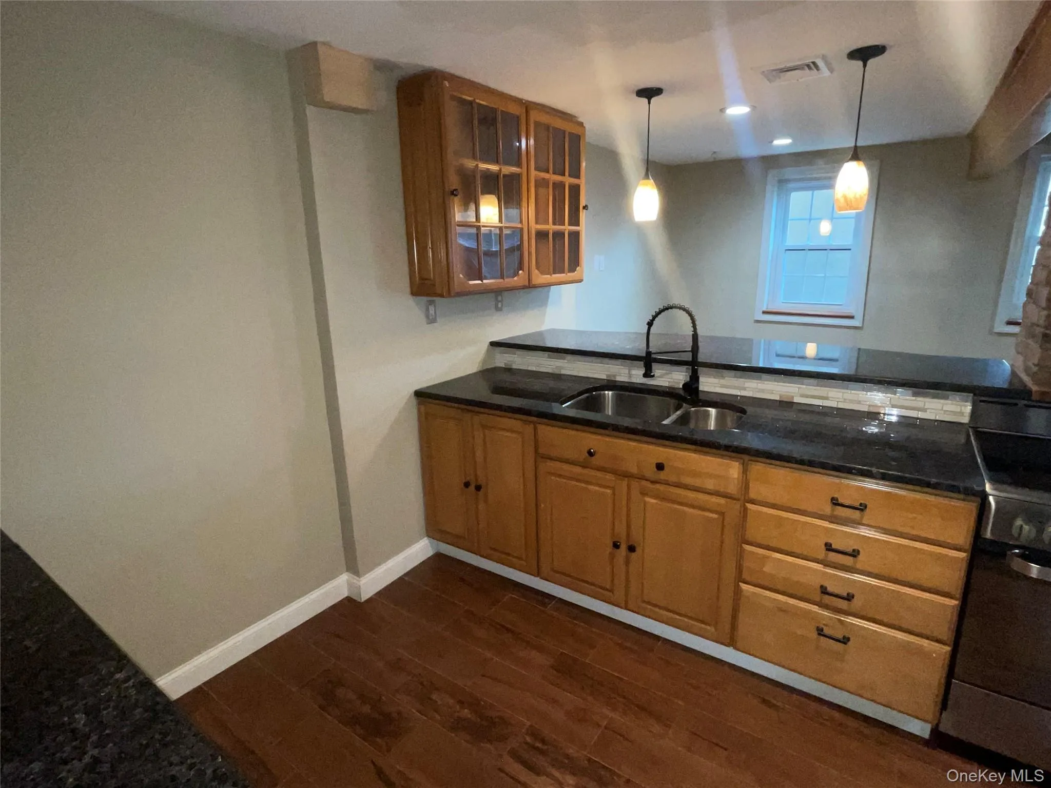 Kitchen with brown cabinetry, stainless steel electric range oven, pendant lighting, dark wood-style floors, and glass insert cabinets Kitchen with brown cabinetry, stainless steel electric range oven, pendant lighting, dark wood-style floors, and glass insert cabinets