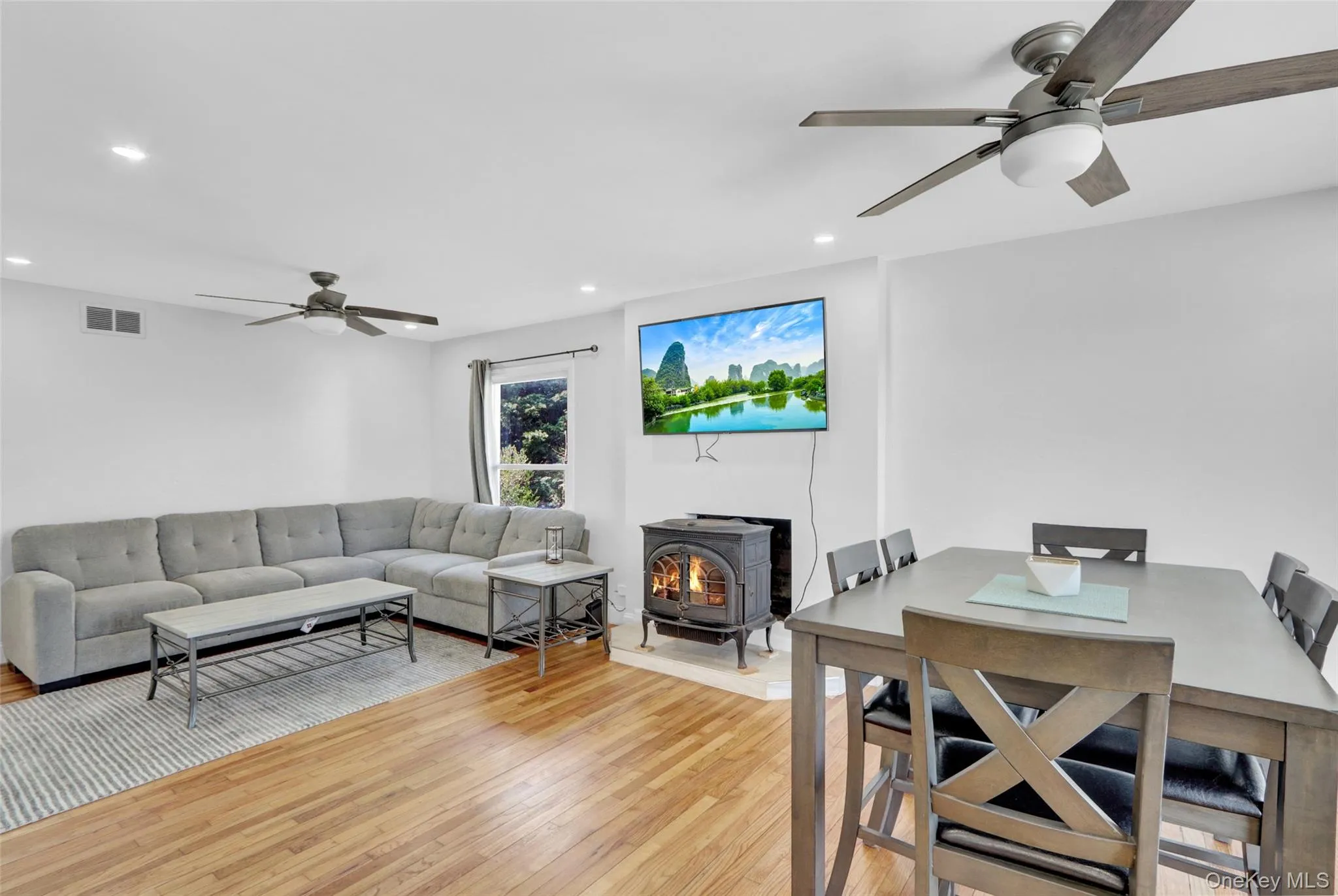 Living area featuring a ceiling fan, a wood stove, light wood finished floors, and recessed lighting Living area featuring a ceiling fan, a wood stove, light wood finished floors, and recessed lighting