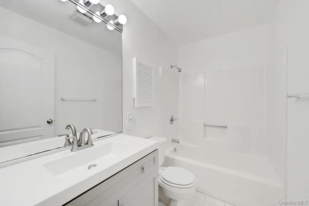 Full bathroom featuring washtub / shower combination, vanity, and light tile patterned floors Full bathroom featuring washtub / shower combination, vanity, and light tile patterned floors