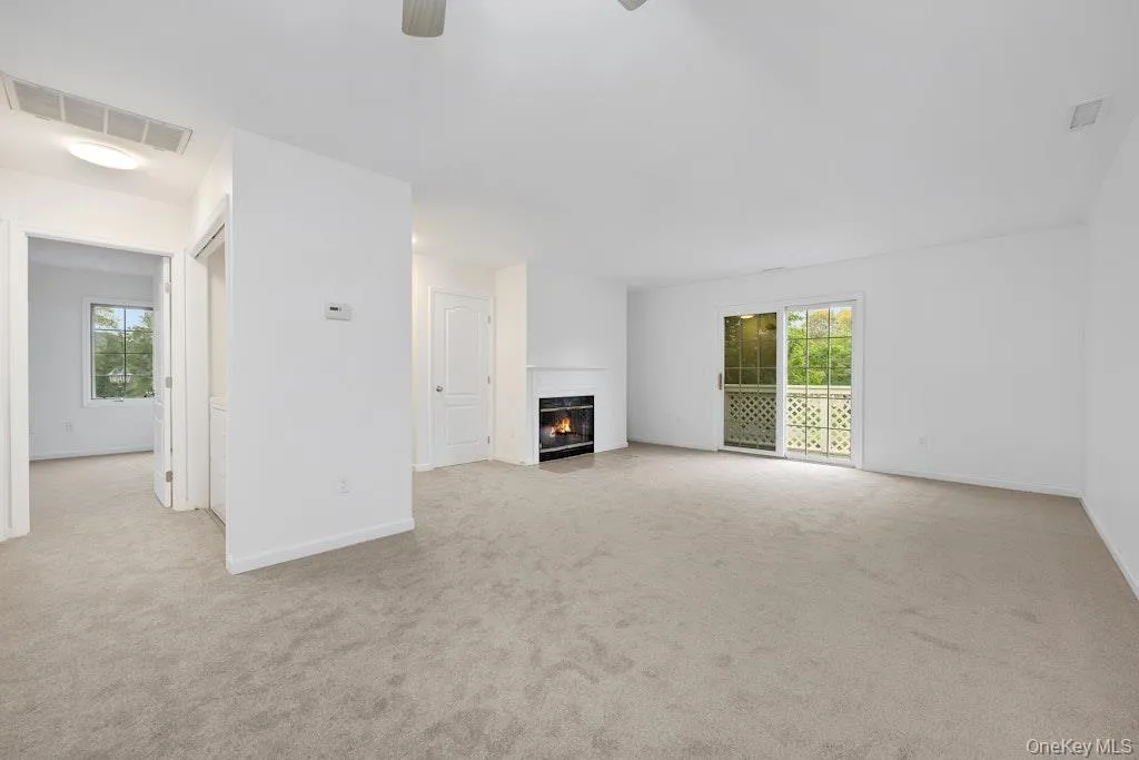 Unfurnished living room with a fireplace with flush hearth, light colored carpet, and a ceiling fan Unfurnished living room with a fireplace with flush hearth, light colored carpet, and a ceiling fan