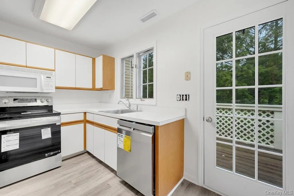 Kitchen featuring appliances with stainless steel finishes, white cabinets, light countertops, and brown cabinets Kitchen featuring appliances with stainless steel finishes, white cabinets, light countertops, and brown cabinets