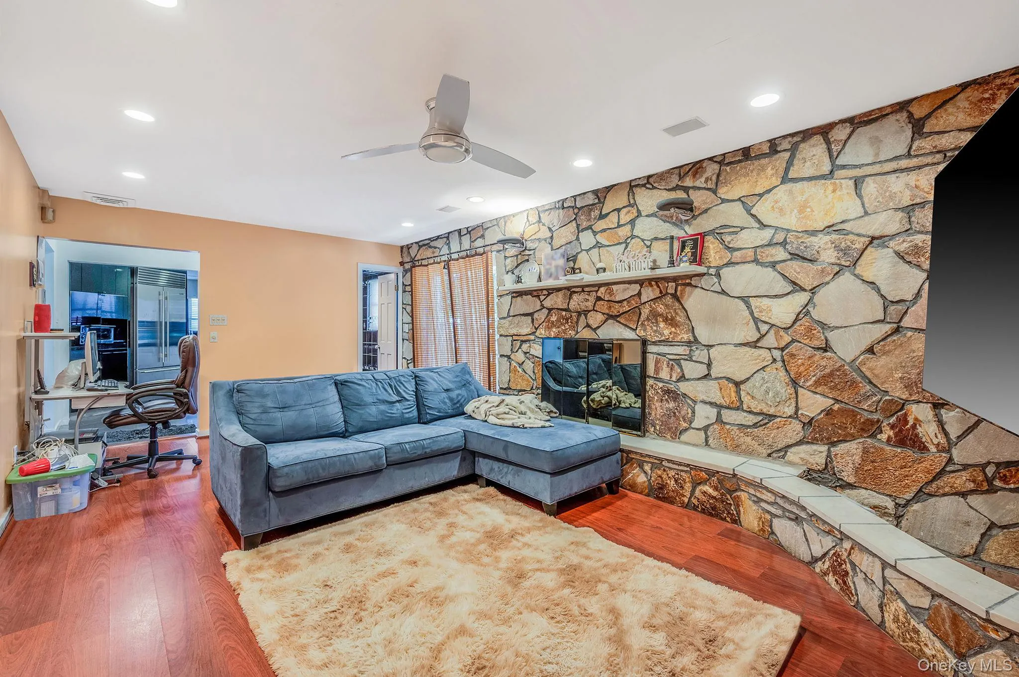 Living room with wood finished floors, a stone fireplace, recessed lighting, and ceiling fan Living room with wood finished floors, a stone fireplace, recessed lighting, and ceiling fan