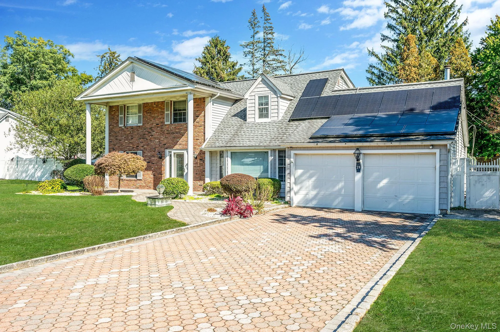 Neoclassical / greek revival house with decorative driveway, solar panels, a shingled roof, an attached garage, and brick siding Neoclassical / greek revival house with decorative driveway, solar panels, a shingled roof, an attached garage, and brick siding