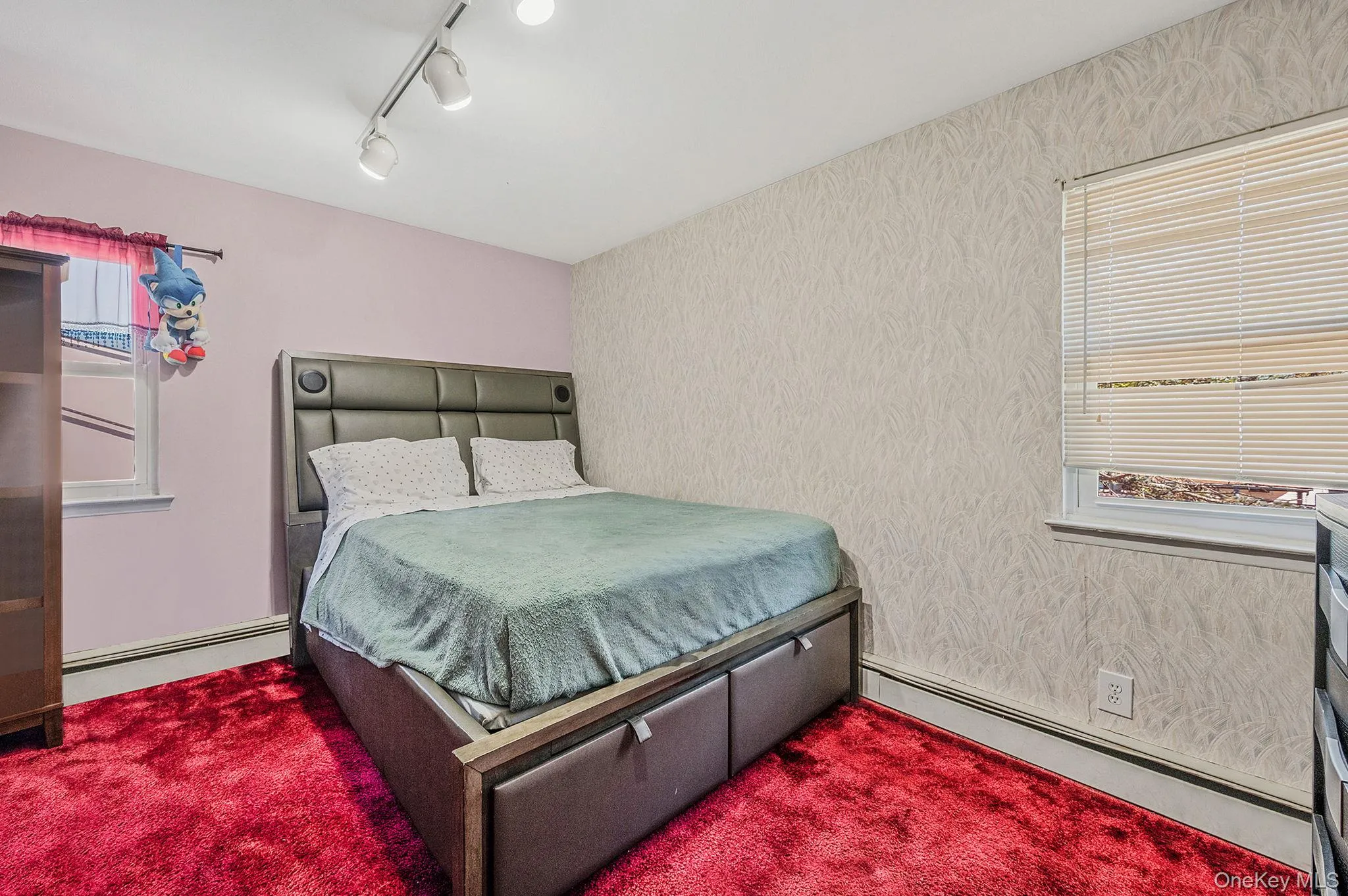 Bedroom with baseboard heating, rail lighting, and wallpapered walls Bedroom with baseboard heating, rail lighting, and wallpapered walls