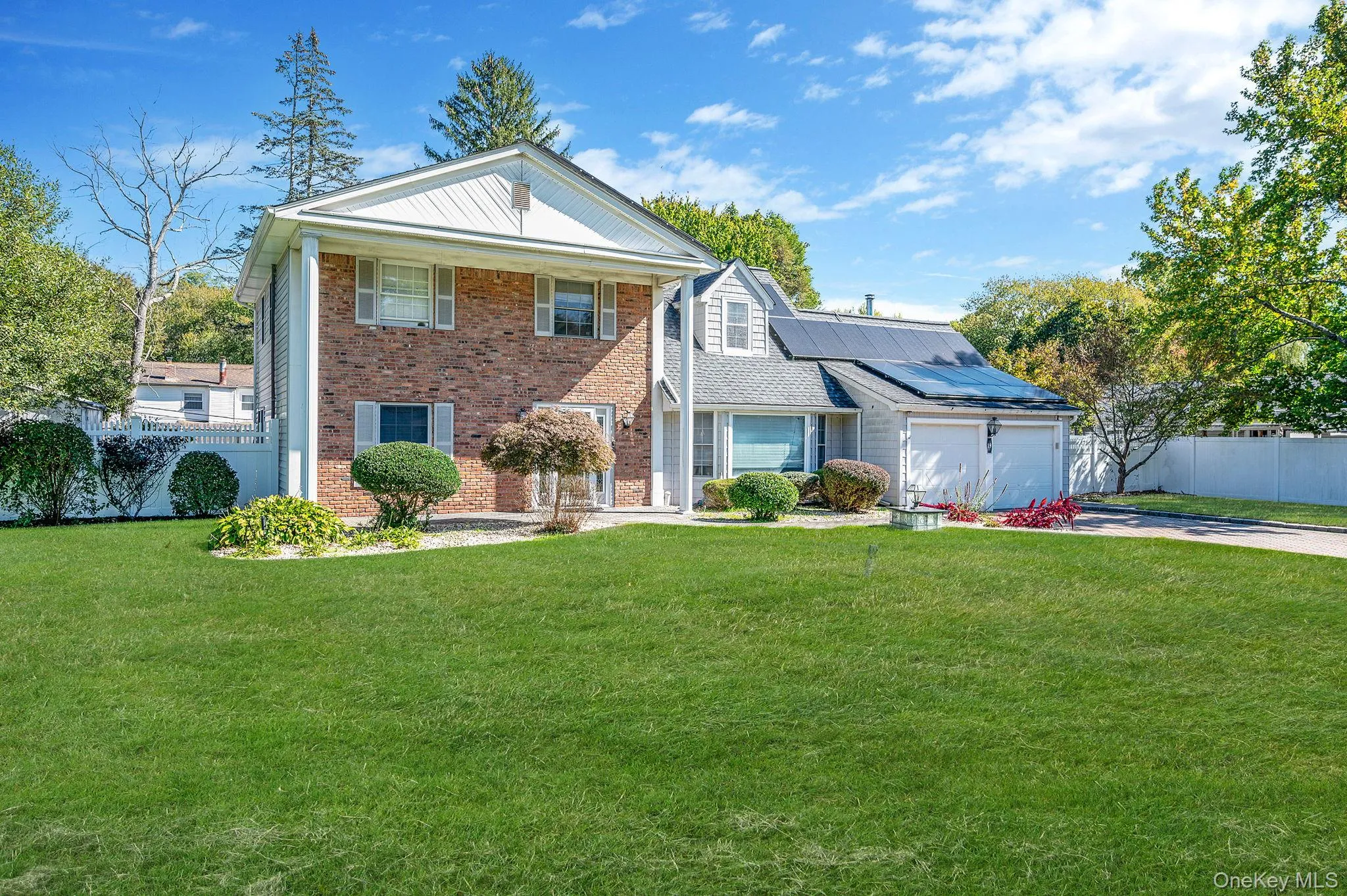 Greek revival house featuring solar panels, brick siding, driveway, a porch, and a garage Greek revival house featuring solar panels, brick siding, driveway, a porch, and a garage