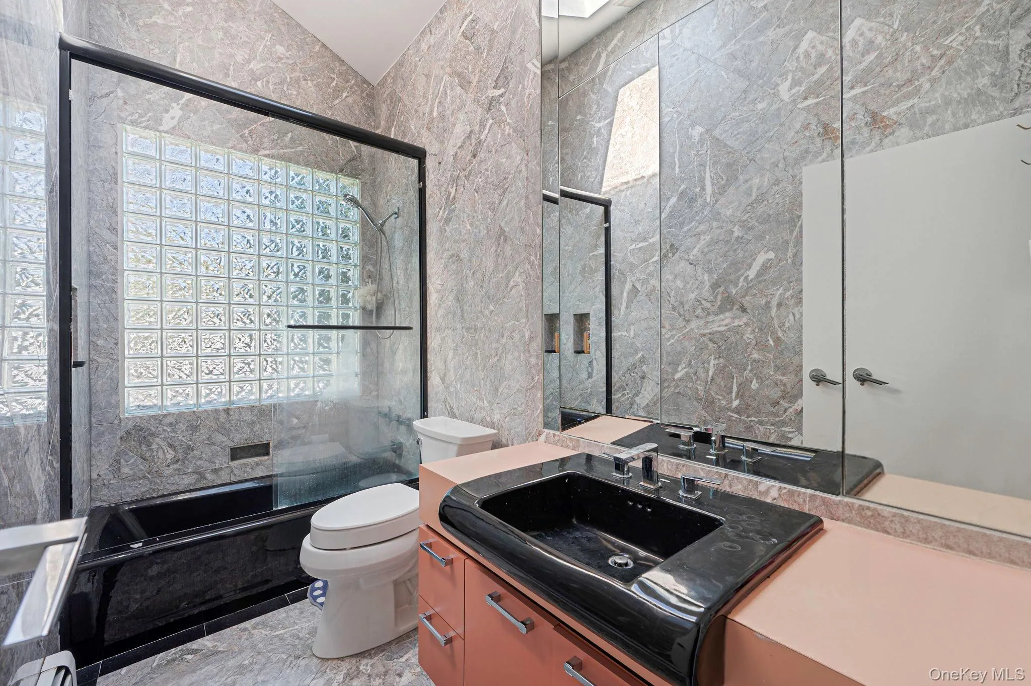 Bathroom with tile walls, vanity, shower / bath combination with glass door, and a baseboard radiator Bathroom with tile walls, vanity, shower / bath combination with glass door, and a baseboard radiator