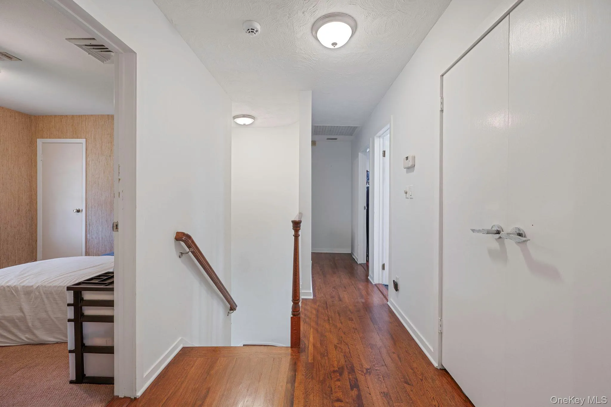 Corridor featuring an upstairs landing, dark wood-style floors, and a textured ceiling Corridor featuring an upstairs landing, dark wood-style floors, and a textured ceiling