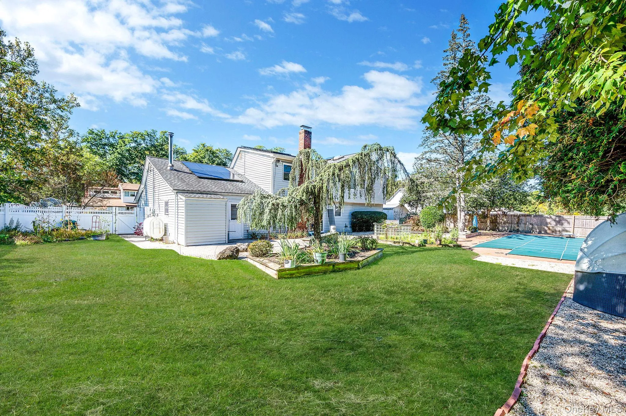Back of house featuring a fenced backyard, roof mounted solar panels, oil tank, a chimney, and a shingled roof Back of house featuring a fenced backyard, roof mounted solar panels, oil tank, a chimney, and a shingled roof