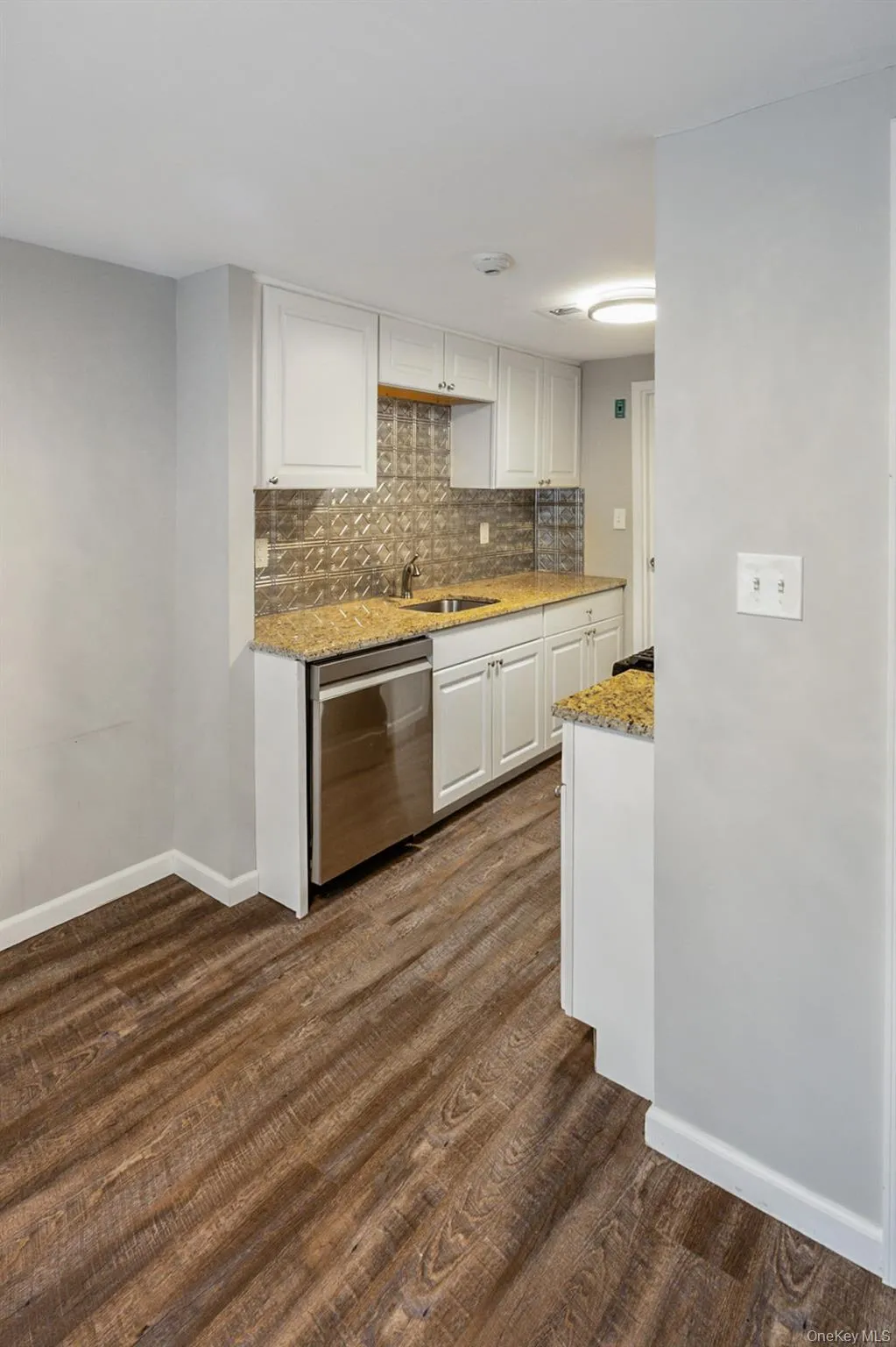 Kitchen featuring white cabinets, light stone counters, stainless steel dishwasher, backsplash, and dark wood-style flooring Kitchen featuring white cabinets, light stone counters, stainless steel dishwasher, backsplash, and dark wood-style flooring