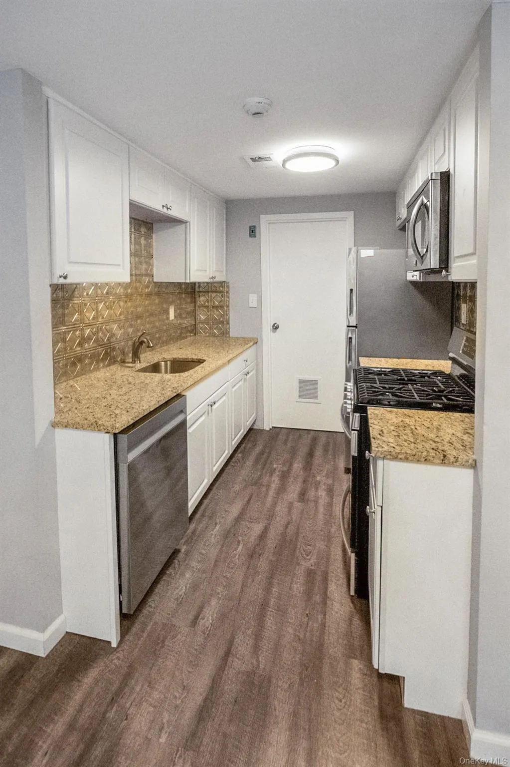 Kitchen featuring appliances with stainless steel finishes, tasteful backsplash, white cabinetry, dark wood-style flooring, and light stone countertops Kitchen featuring appliances with stainless steel finishes, tasteful backsplash, white cabinetry, dark wood-style flooring, and light stone countertops