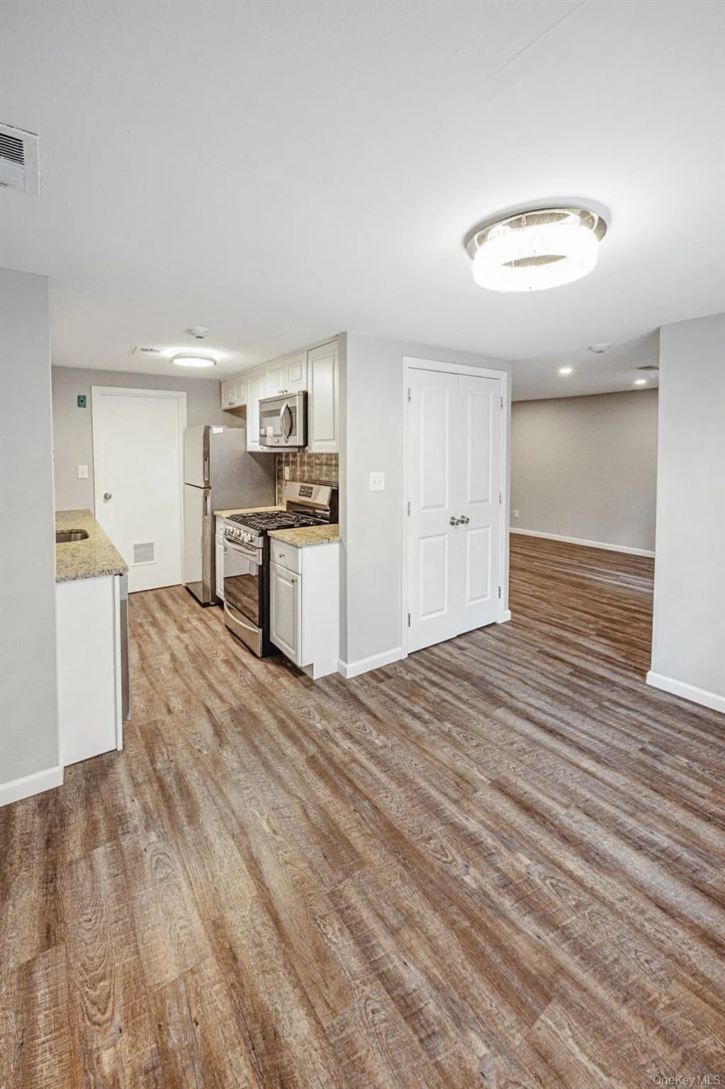 Kitchen with appliances with stainless steel finishes, light wood finished floors, light stone counters, white cabinetry, and tasteful backsplash Kitchen with appliances with stainless steel finishes, light wood finished floors, light stone counters, white cabinetry, and tasteful backsplash