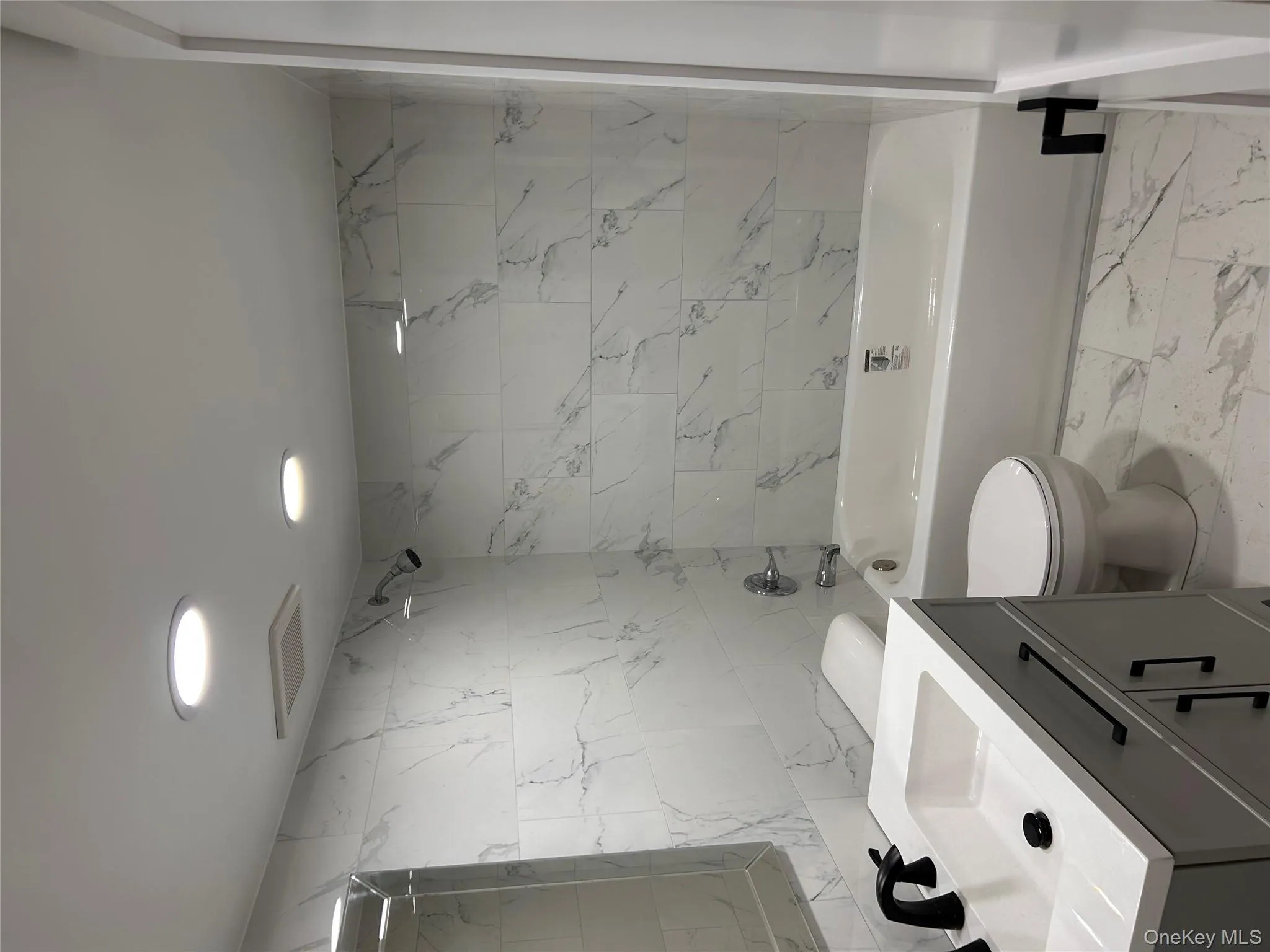 Full bath featuring shower / washtub combination, light marble finish flooring, vanity, tile walls, and recessed lighting Full bath featuring shower / washtub combination, light marble finish flooring, vanity, tile walls, and recessed lighting