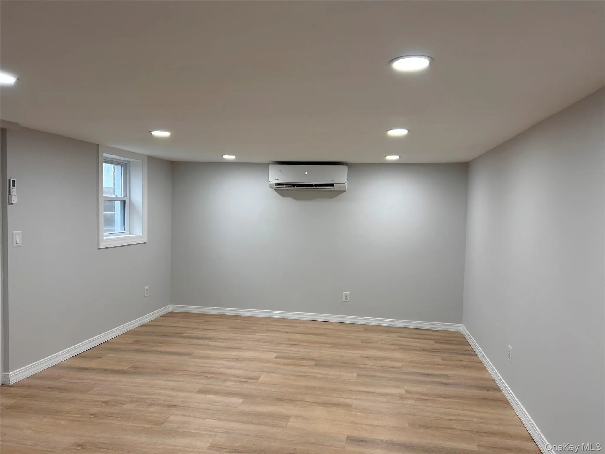 Below grade area featuring light wood-style flooring, recessed lighting, and an AC wall unit Below grade area featuring light wood-style flooring, recessed lighting, and an AC wall unit