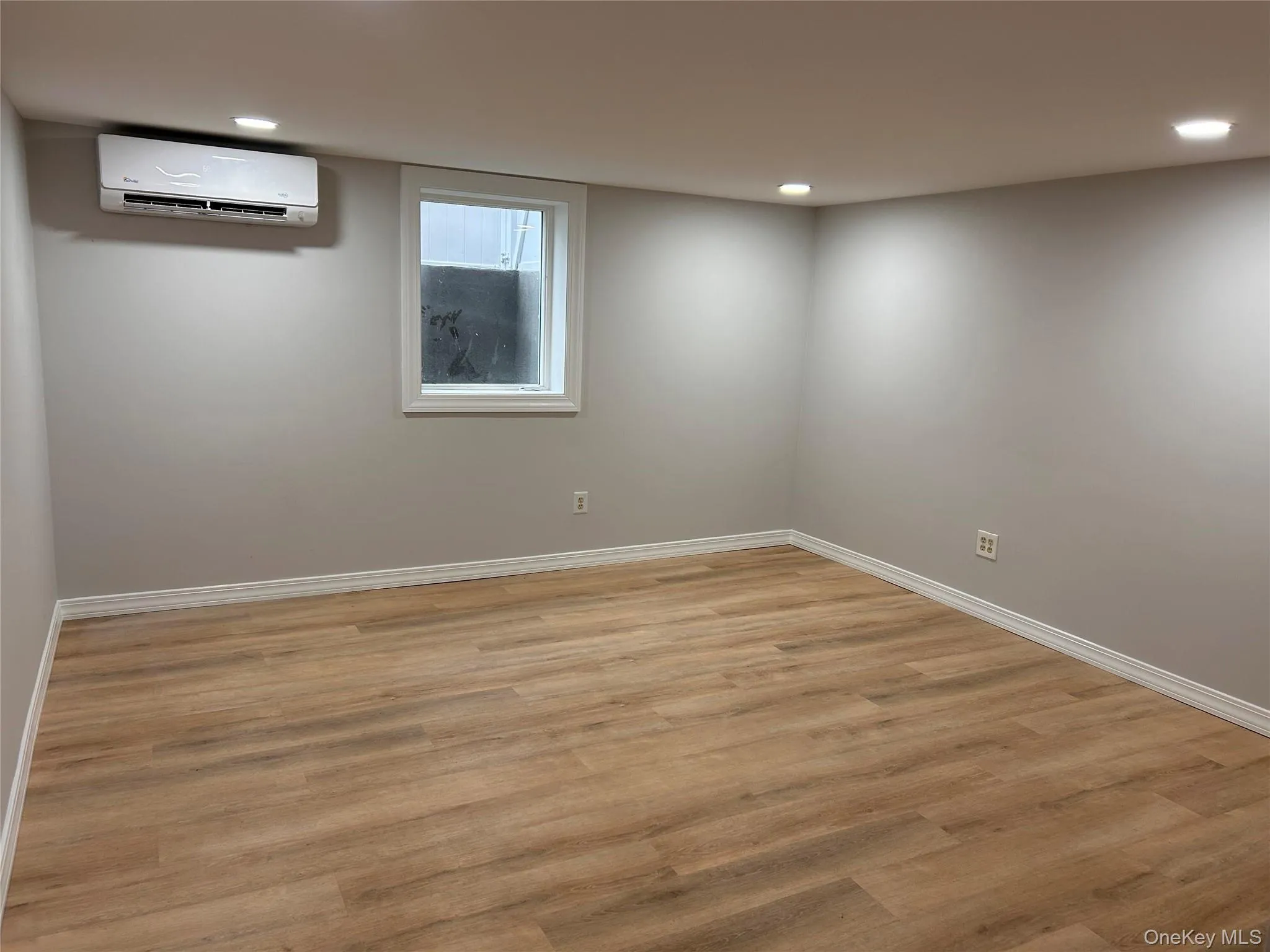 Empty room featuring light wood-type flooring, a wall unit AC, and recessed lighting Empty room featuring light wood-type flooring, a wall unit AC, and recessed lighting