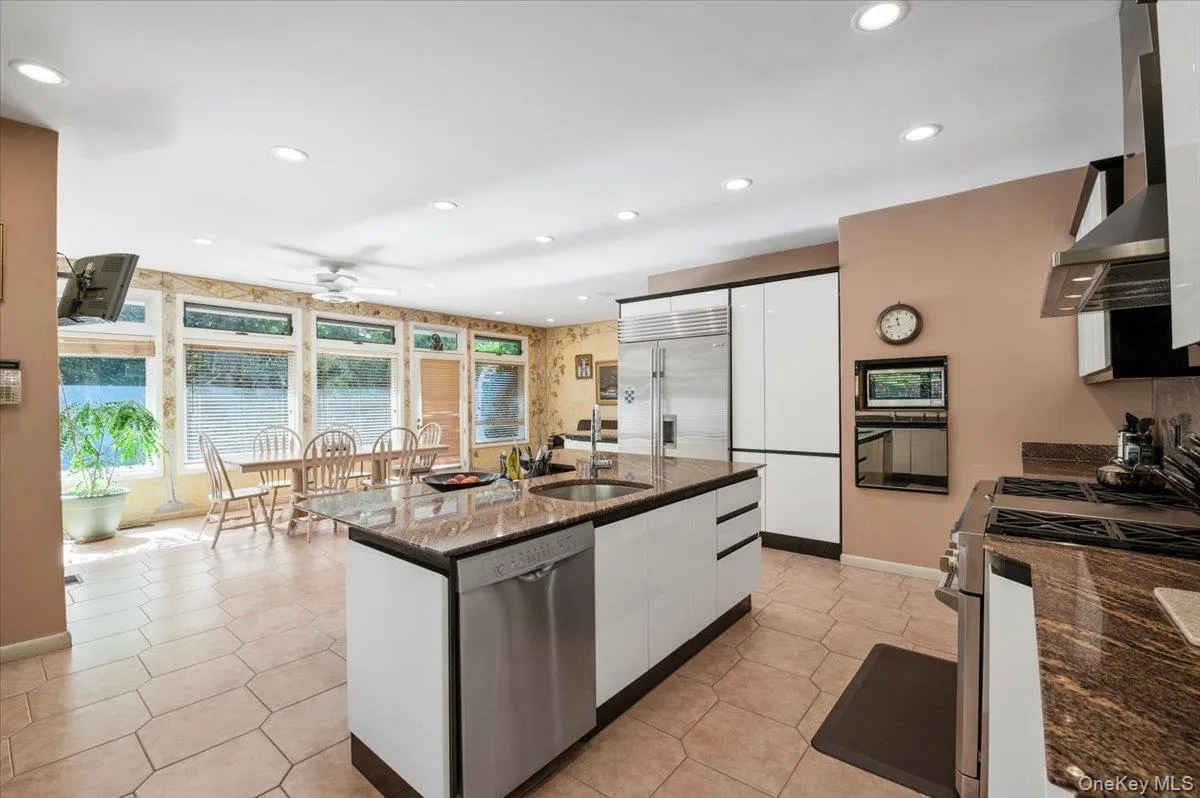 Kitchen featuring stainless steel appliances, white cabinets, wall chimney exhaust hood, dark stone counters, and modern cabinets Kitchen featuring stainless steel appliances, white cabinets, wall chimney exhaust hood, dark stone counters, and modern cabinets