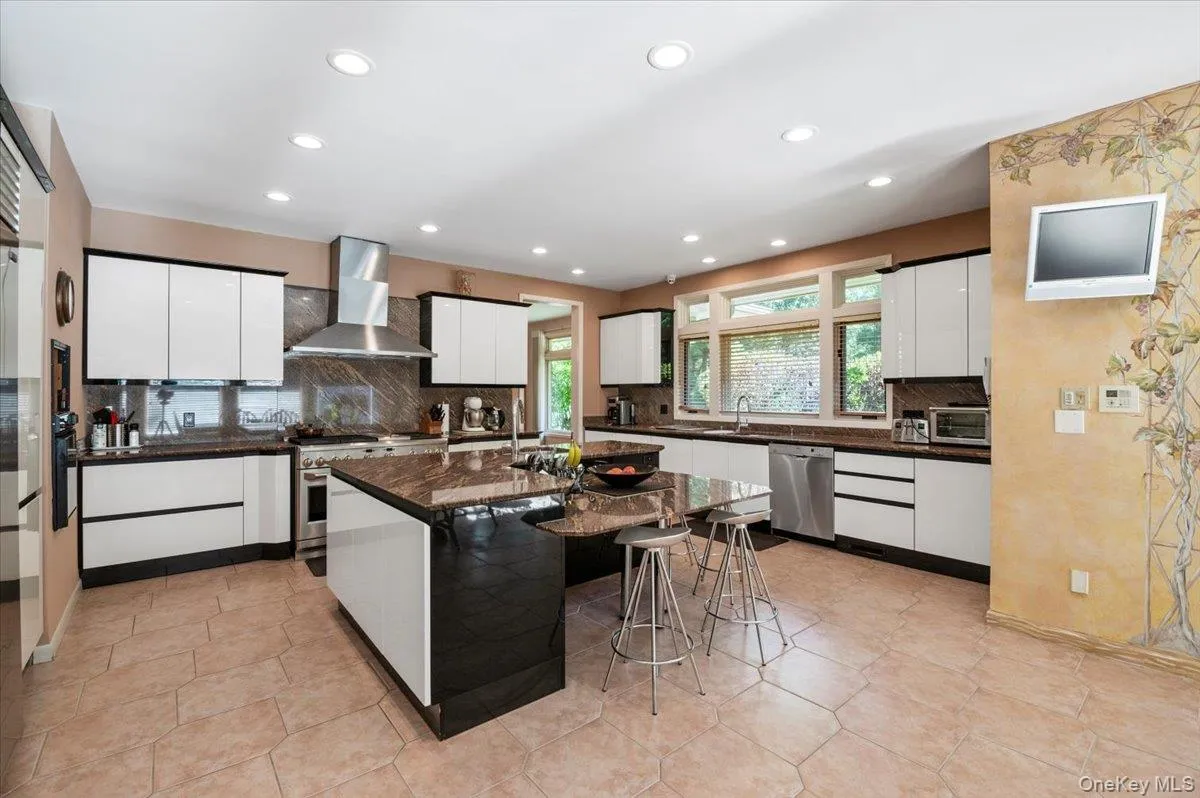 Kitchen featuring white cabinetry, wall chimney range hood, tasteful backsplash, high quality appliances, and an island with sink Kitchen featuring white cabinetry, wall chimney range hood, tasteful backsplash, high quality appliances, and an island with sink