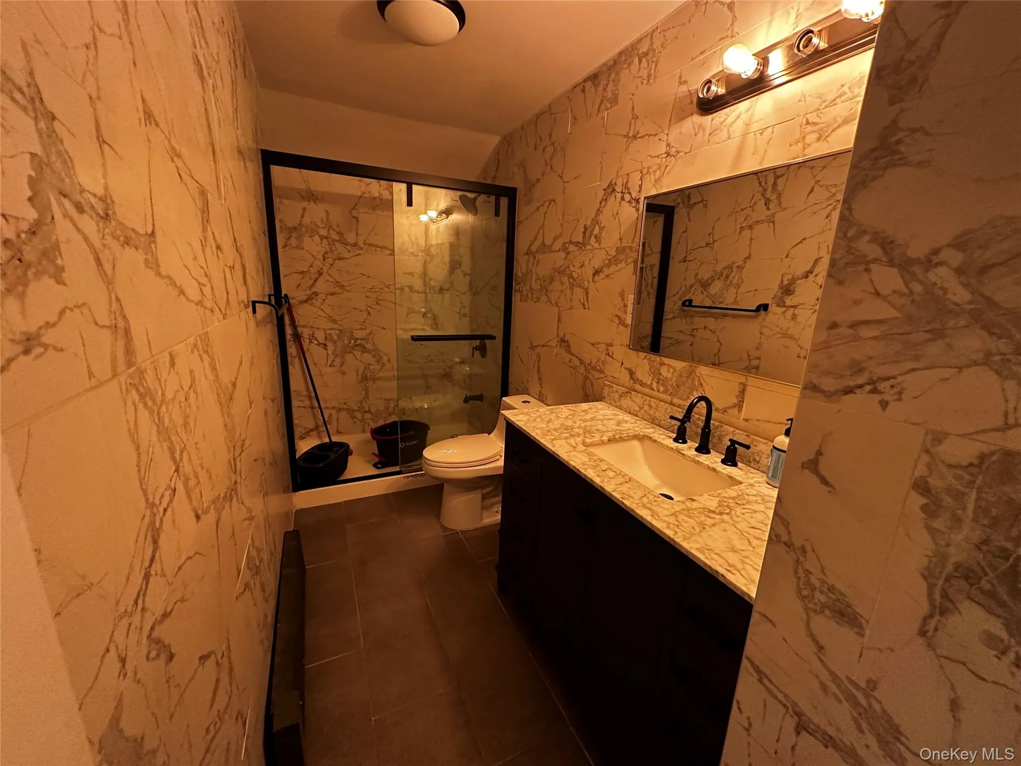 Full bath with tile walls, a marble finish shower, vanity, dark tile patterned floors, and stone wall Full bath with tile walls, a marble finish shower, vanity, dark tile patterned floors, and stone wall