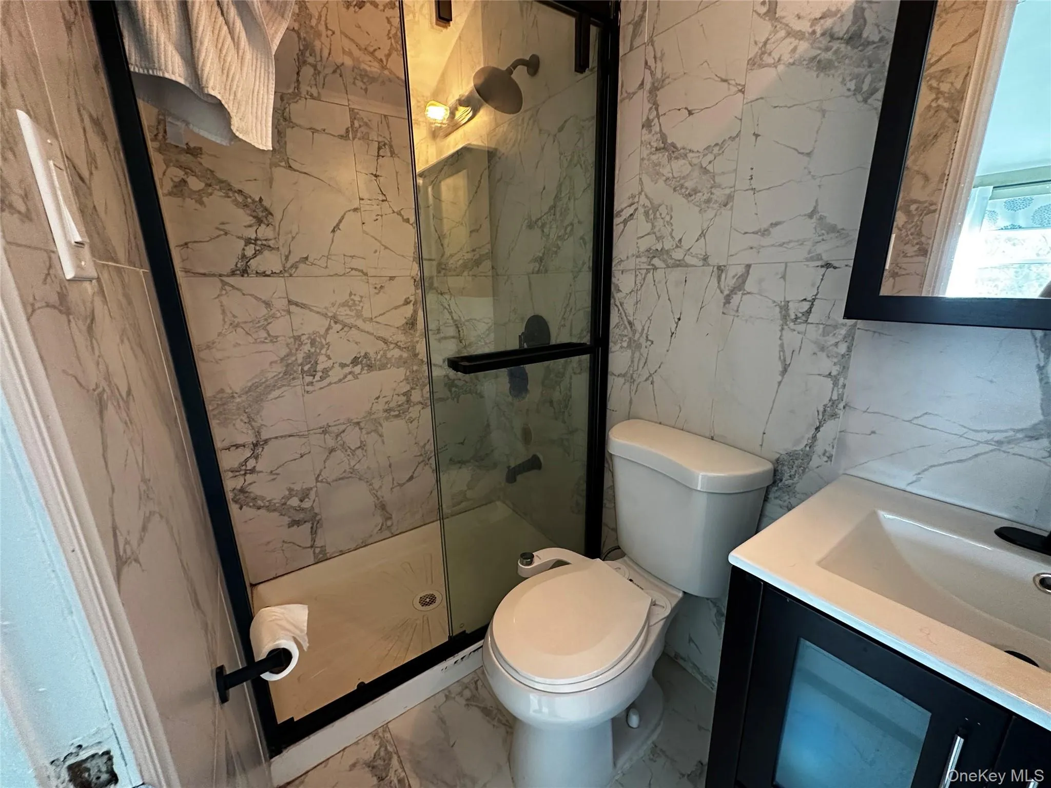 Full bathroom with a marble finish shower, vanity, tile walls, and marble finish flooring Full bathroom with a marble finish shower, vanity, tile walls, and marble finish flooring
