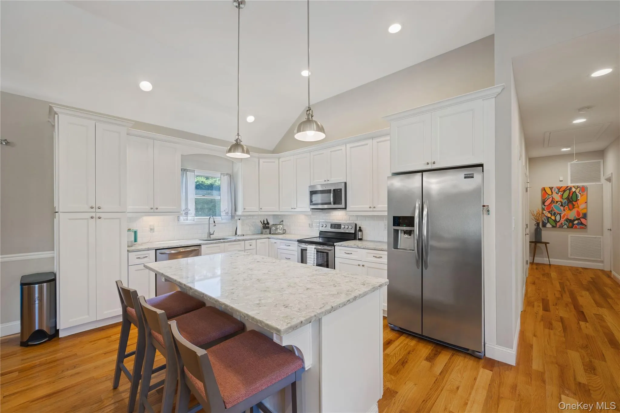 Kitchen featuring stainless steel appliances, lofted ceiling, a kitchen island, white cabinetry, and a kitchen breakfast bar Kitchen featuring stainless steel appliances, lofted ceiling, a kitchen island, white cabinetry, and a kitchen breakfast bar