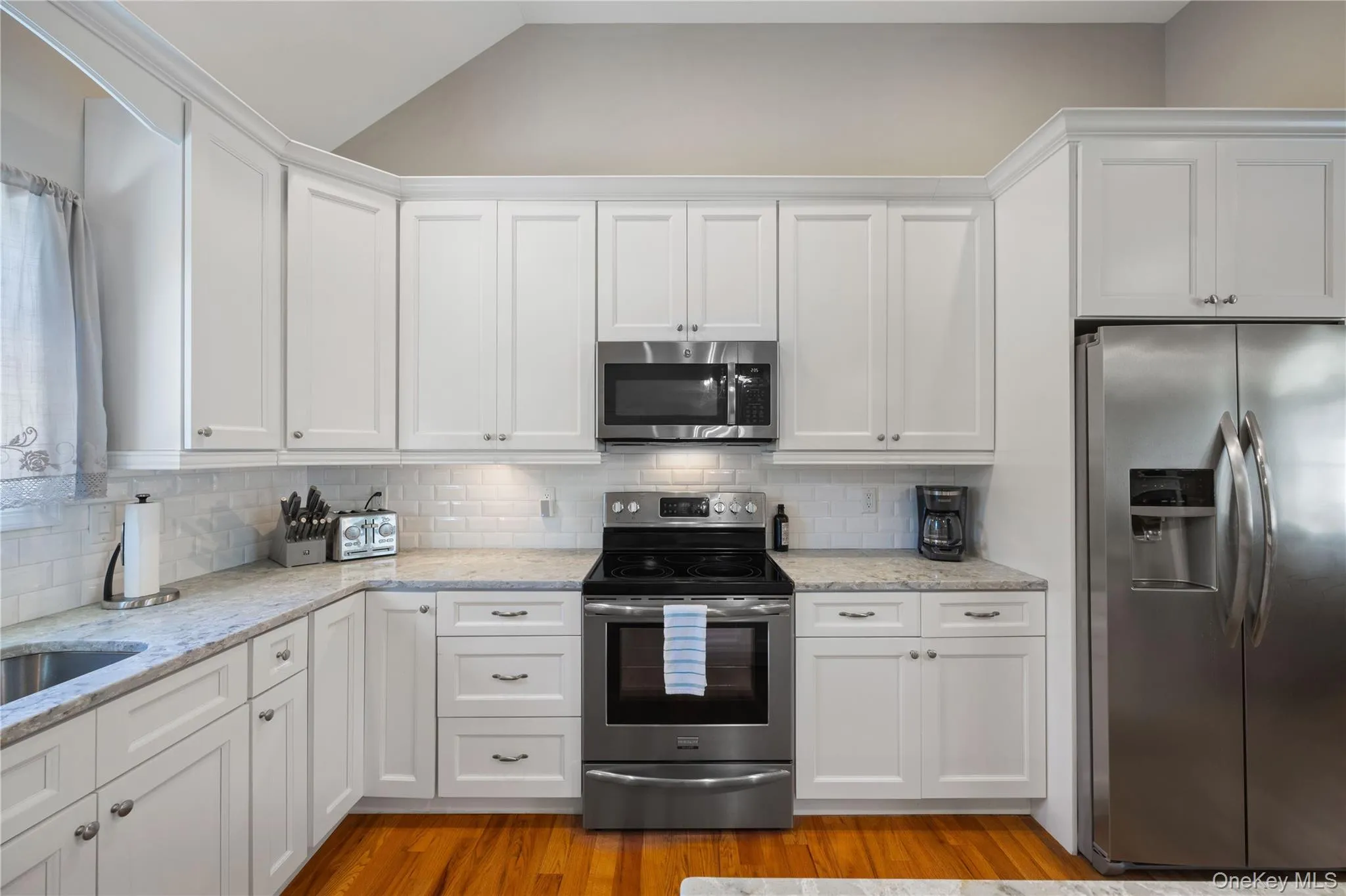 Kitchen featuring stainless steel appliances, white cabinetry, decorative backsplash, light stone counters, and light wood-type flooring Kitchen featuring stainless steel appliances, white cabinetry, decorative backsplash, light stone counters, and light wood-type flooring