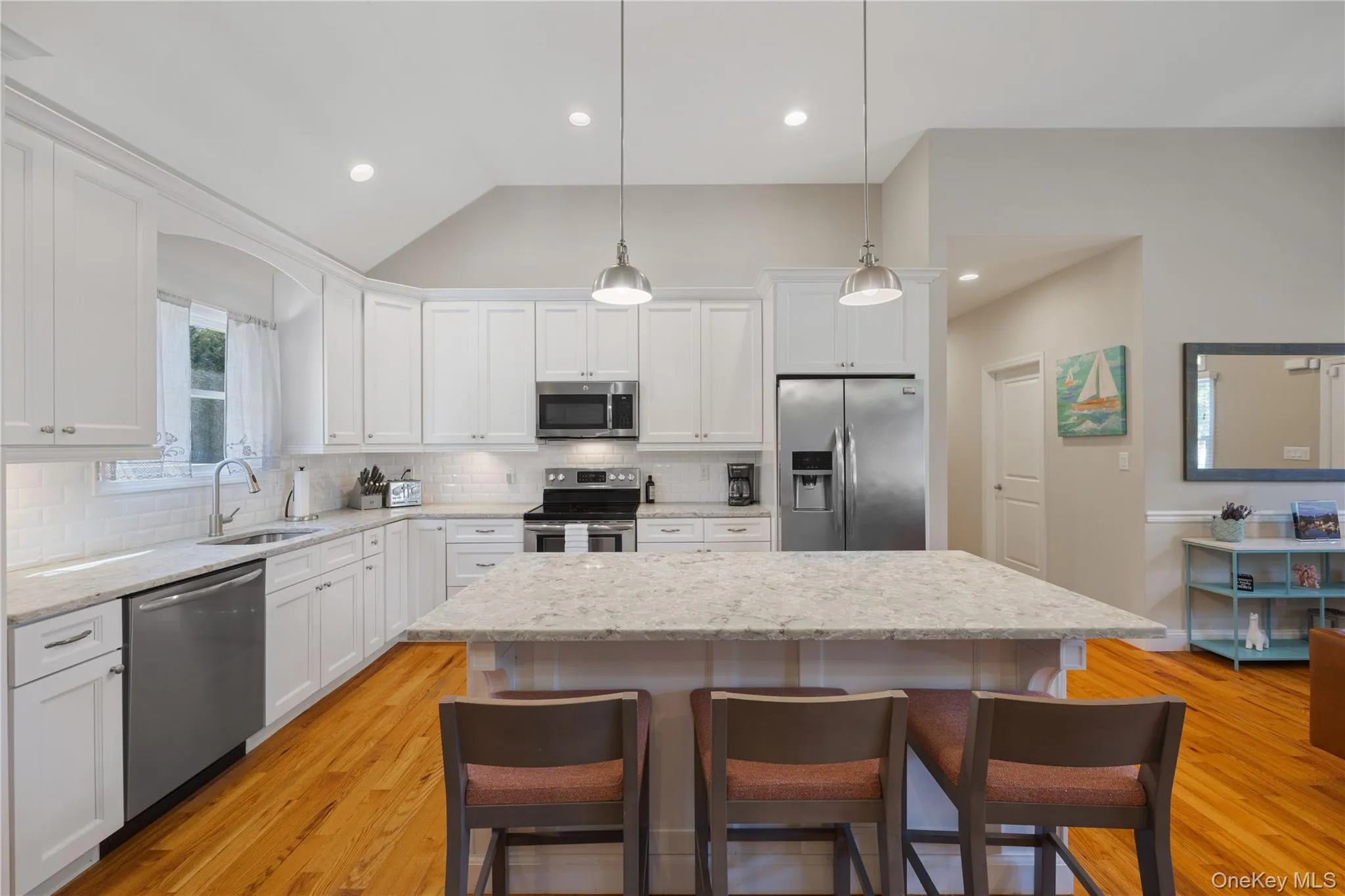 Kitchen with a breakfast bar area, vaulted ceiling, stainless steel appliances, white cabinets, and decorative backsplash Kitchen with a breakfast bar area, vaulted ceiling, stainless steel appliances, white cabinets, and decorative backsplash