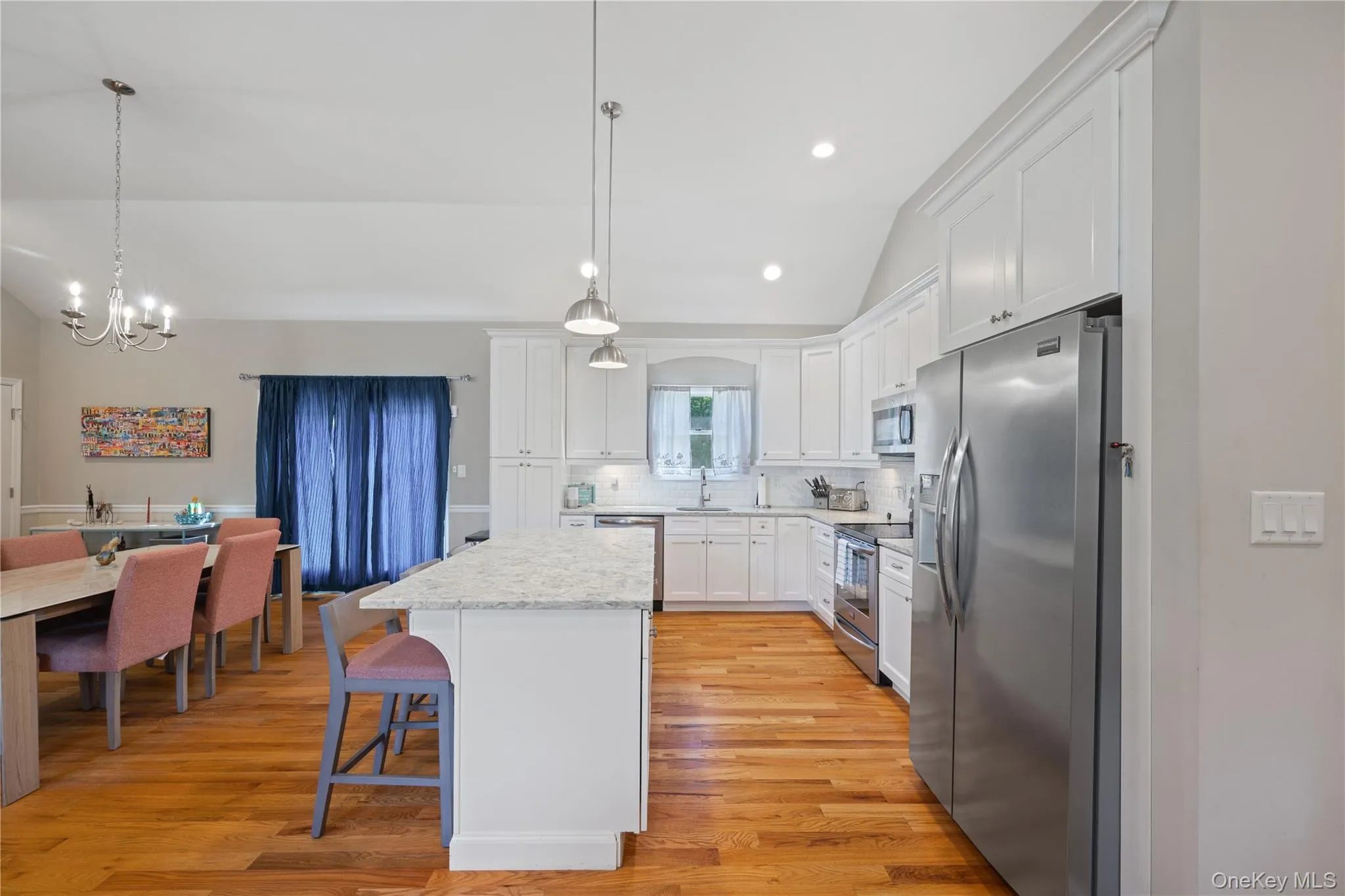 Kitchen featuring lofted ceiling, appliances with stainless steel finishes, white cabinetry, tasteful backsplash, and light wood-style flooring Kitchen featuring lofted ceiling, appliances with stainless steel finishes, white cabinetry, tasteful backsplash, and light wood-style flooring