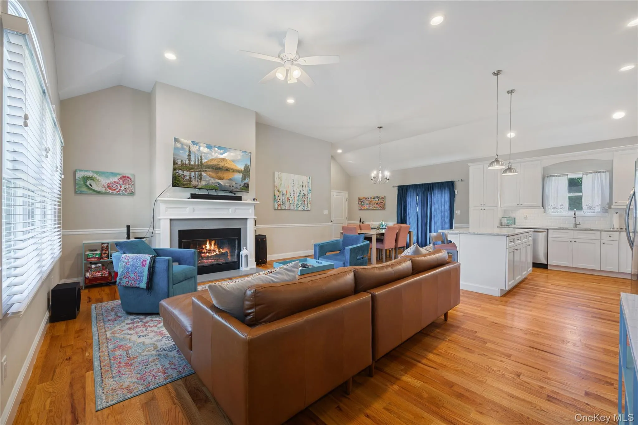 Living area featuring lofted ceiling, light wood-style floors, a fireplace with flush hearth, recessed lighting, and ceiling fan Living area featuring lofted ceiling, light wood-style floors, a fireplace with flush hearth, recessed lighting, and ceiling fan