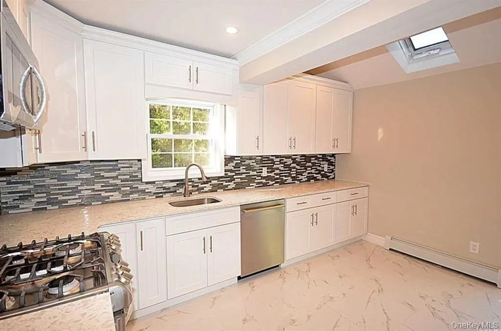 Kitchen featuring white cabinetry, appliances with stainless steel finishes, a baseboard radiator, decorative backsplash, and crown molding Kitchen featuring white cabinetry, appliances with stainless steel finishes, a baseboard radiator, decorative backsplash, and crown molding