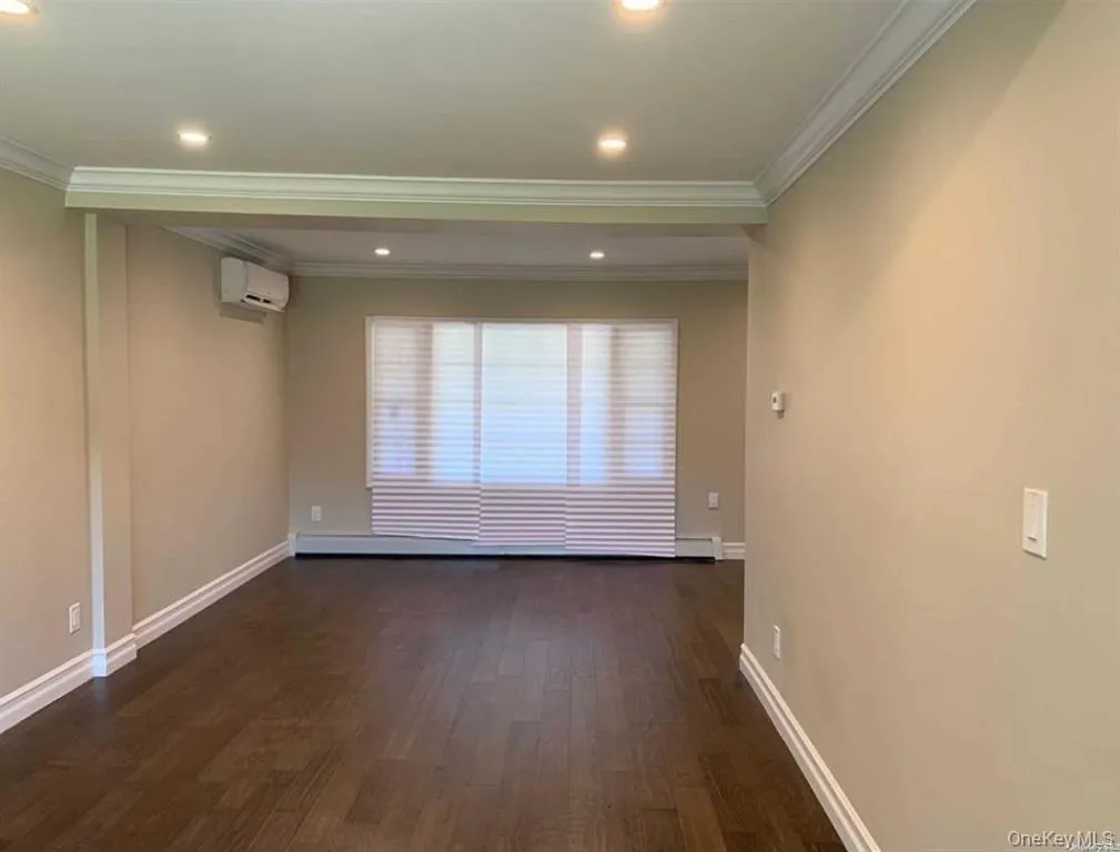 Empty room with dark wood-style floors, ornamental molding, recessed lighting, and an AC wall unit Empty room with dark wood-style floors, ornamental molding, recessed lighting, and an AC wall unit