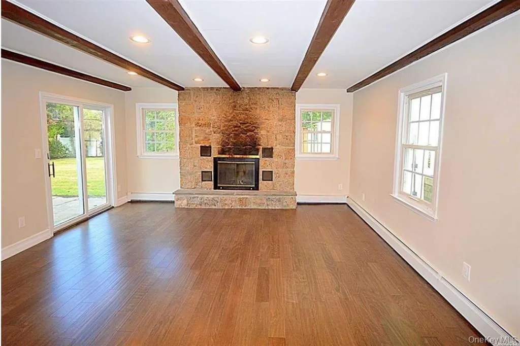 Unfurnished living room with baseboard heating, beam ceiling, dark wood finished floors, a fireplace, and recessed lighting Unfurnished living room with baseboard heating, beam ceiling, dark wood finished floors, a fireplace, and recessed lighting