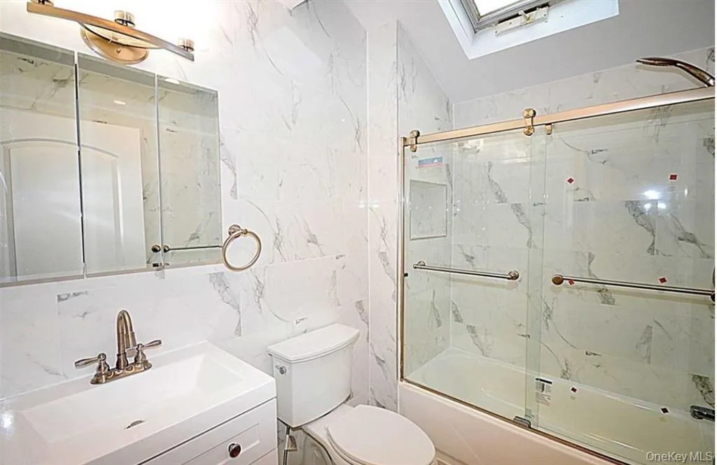 Bathroom featuring tile walls, bath / shower combo with glass door, vanity, a skylight, and backsplash Bathroom featuring tile walls, bath / shower combo with glass door, vanity, a skylight, and backsplash