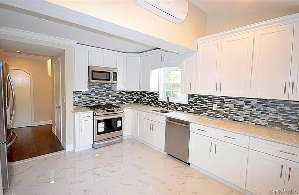 Kitchen with light marble finish floors, white cabinets, appliances with stainless steel finishes, tasteful backsplash, and ornamental molding Kitchen with light marble finish floors, white cabinets, appliances with stainless steel finishes, tasteful backsplash, and ornamental molding