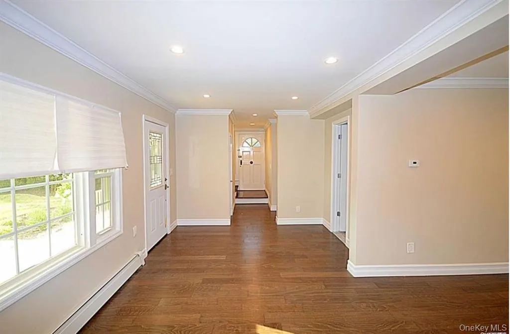 Hallway with a baseboard heating unit, ornamental molding, dark wood-type flooring, and recessed lighting Hallway with a baseboard heating unit, ornamental molding, dark wood-type flooring, and recessed lighting