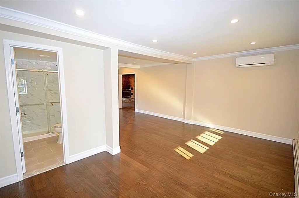 Empty room featuring crown molding, recessed lighting, dark wood-style floors, a wall mounted AC, and baseboard heating Empty room featuring crown molding, recessed lighting, dark wood-style floors, a wall mounted AC, and baseboard heating