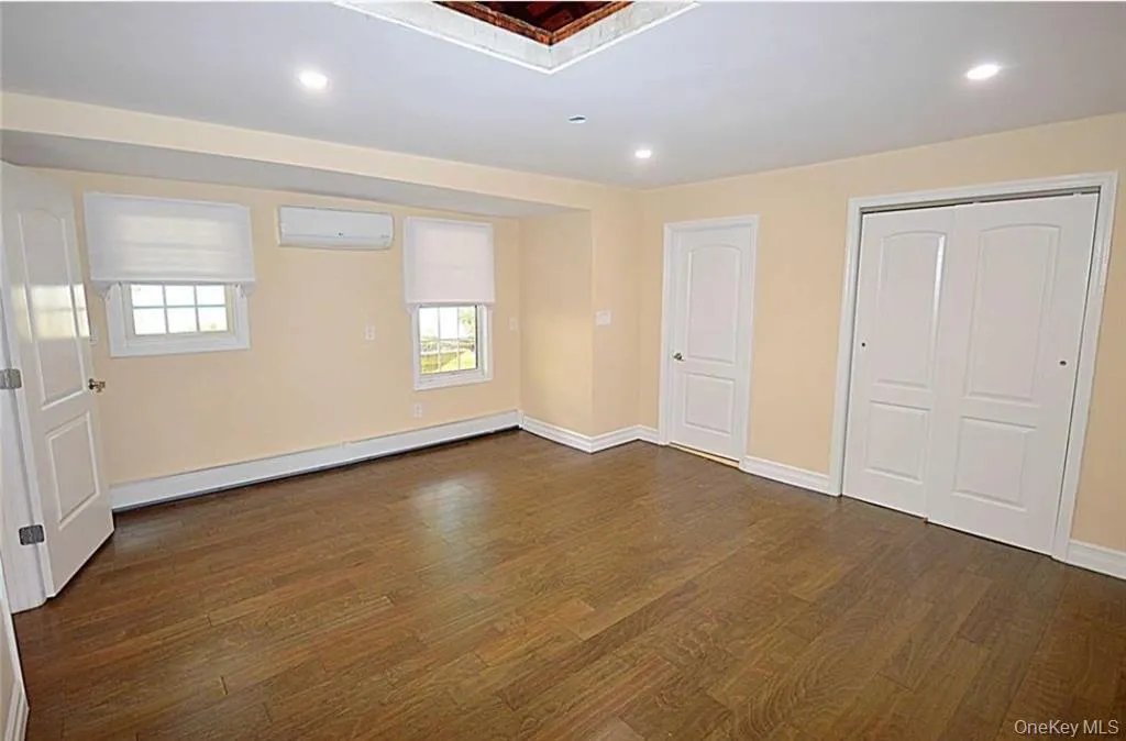 Unfurnished bedroom with recessed lighting, multiple windows, dark wood finished floors, a baseboard heating unit, and a closet Unfurnished bedroom with recessed lighting, multiple windows, dark wood finished floors, a baseboard heating unit, and a closet