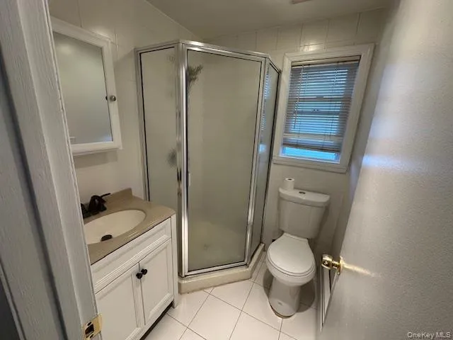 Full bath with vanity, a stall shower, light tile patterned flooring, and tile walls Full bath with vanity, a stall shower, light tile patterned flooring, and tile walls