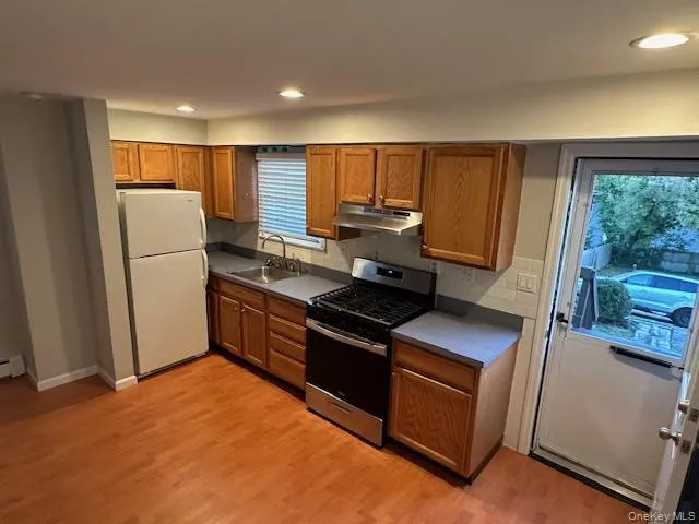 Kitchen featuring stainless steel gas stove, brown cabinets, freestanding refrigerator, and recessed lighting Kitchen featuring stainless steel gas stove, brown cabinets, freestanding refrigerator, and recessed lighting