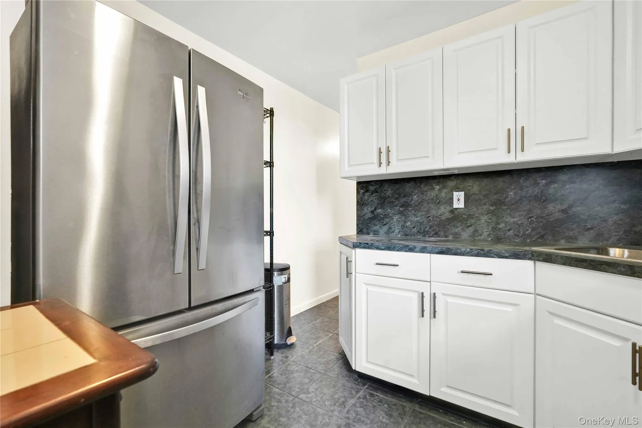 Kitchen with freestanding refrigerator, white cabinets, dark countertops, tasteful backsplash, and dark tile patterned floors Kitchen with freestanding refrigerator, white cabinets, dark countertops, tasteful backsplash, and dark tile patterned floors